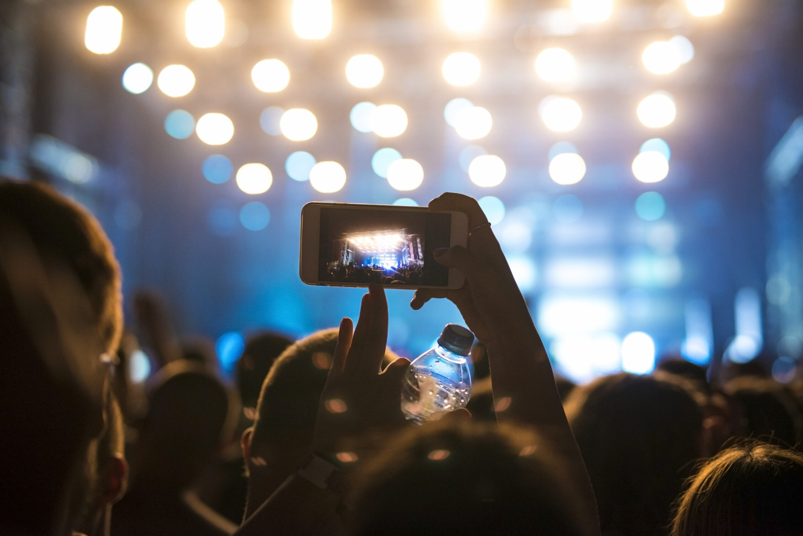 Woman in the crowd taking picture of stage at music festival.